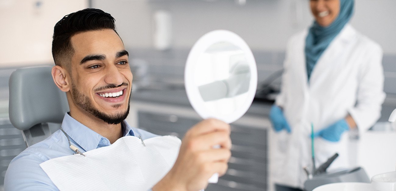 Man in dental chair smiling at reflection in mirror with dentist in background
