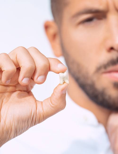 Man holding extracted tooth and touching jaw in pain
