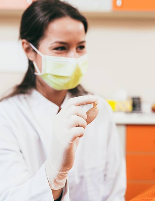 Dentist in yellow mask showing patient her extracted tooth