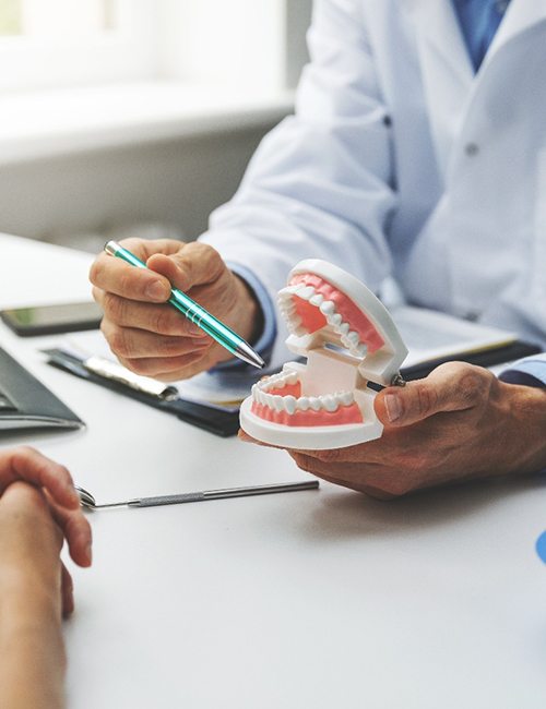 Dentist pointing to model of teeth in office