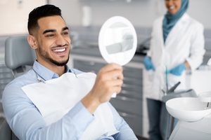 Man in dental chair smiling at reflection in mirror with dentist in background